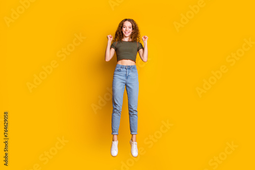 Full length photo of glad optimistic girl dressed stylish clothes raise hands celebrating achievement isolated on yellow color background
