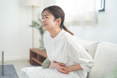 Konstfotografi ソファに座りお腹の痛みを訴えるミドルの女性