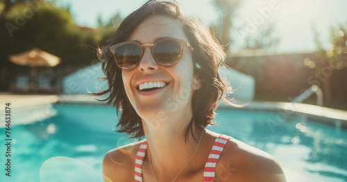 Lifestyle portrait of happy brunette woman wearing striped swimsuit, laughing and swimming in resort pool on holiday