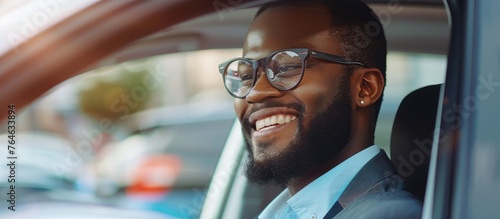A smiling man with a beard wearing glasses inside a car © 2rogan