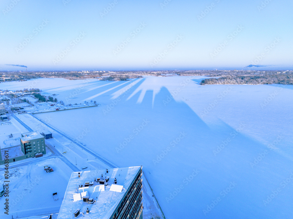 Aerial view over the frozen sea with the shadow of the tower of Helsinki