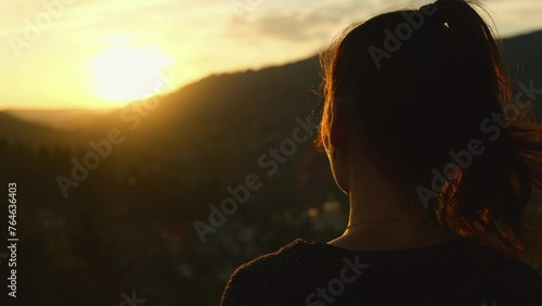Young woman enjoying sunset in mountains. Female hiker portrait looking at beautiful sunrise above valley at the foot of the mountains scenic landscape