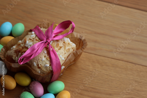 Sweet Easter cake named Colomba Pasquale (Easter dove) with pink tied bow, chocolate eggs  on wooden table. Italian traditional pastry 