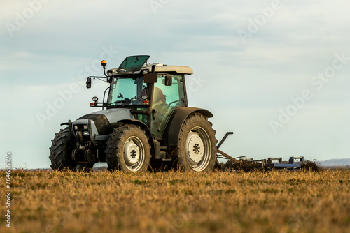Modern tractor actively plows through farmland, creating a dynamic scene amidst an evening backdrop © oticki