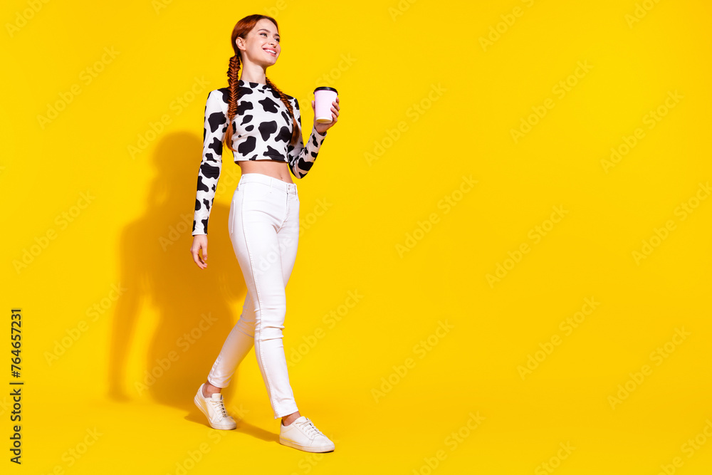 Full length photo of dreamy cute lady dressed cowskin print top enjoying milk walking empty space isolated yellow color background - obrazy, fototapety, plakaty 