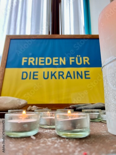 A sign reads in German: Peace for Ukraine. There are lit candles in the foreground. Concept: war and peace
