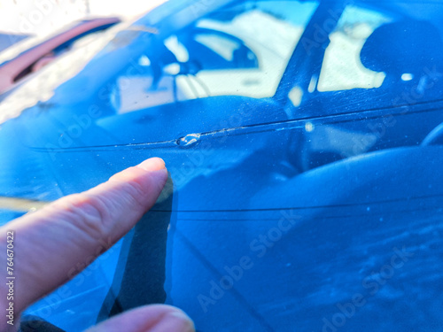 Woman Pointing Out Chip on Her Car's Windshield in Bright Daylight. A finger indicating a small chip on a vehicles windshield