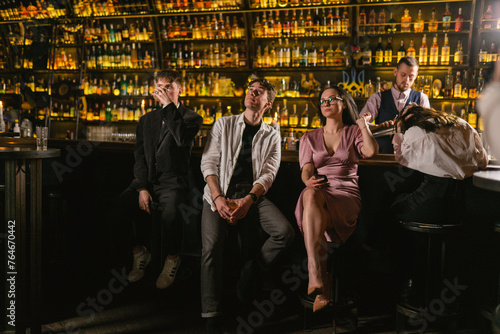 Ladies and men tired after noisy party and sit in quiet place. Bartender makes drinks for tired company after party in fancy pub