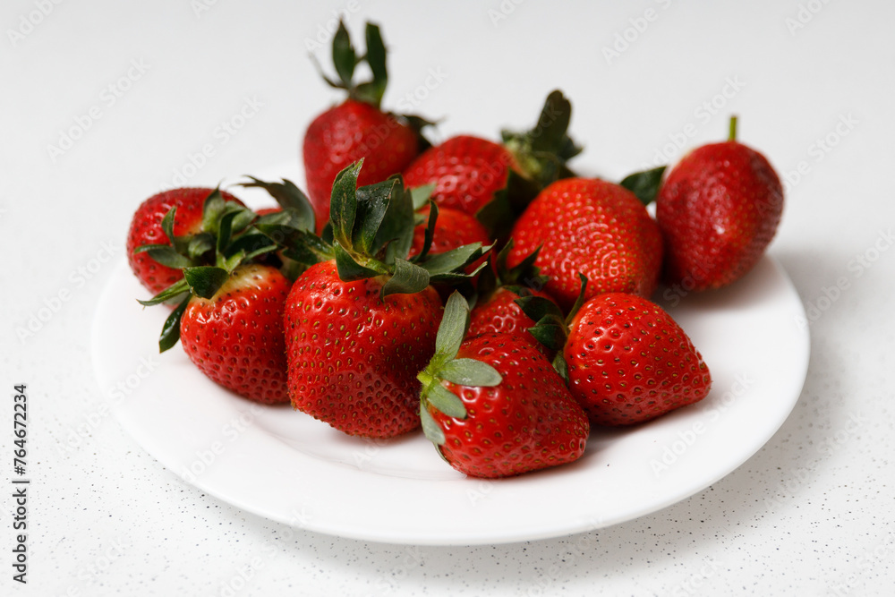 Juicy red strawberries lie on a white saucer Juicy red strawberries lie on a white saucer