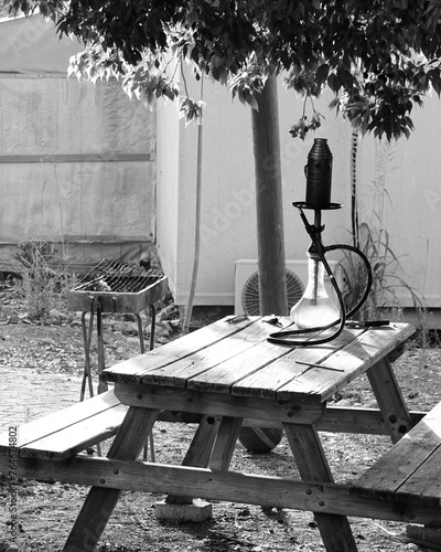 Rustic Backyard Relaxation In Black And White. Wooden Picnic Table And Vintage Lantern Create A Quaint Outdoor Scene