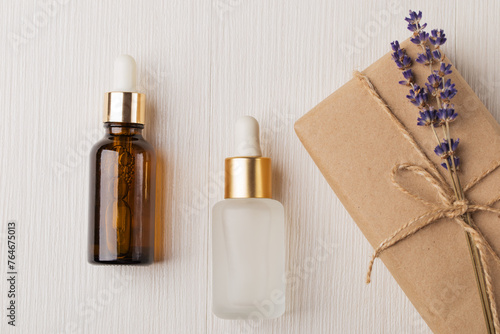 Flat lay composition with lavender cosmetic oil, face serum, eco friendly gift box with lavender bouquet on white wooden table. Herbal cosmetics and aromatherapy concept. Lavender beauty products.