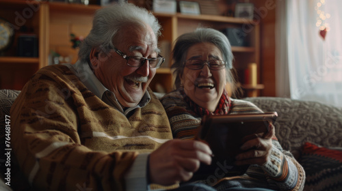 Two joyous seniors share a laugh while looking at a tablet in a cozy living room.