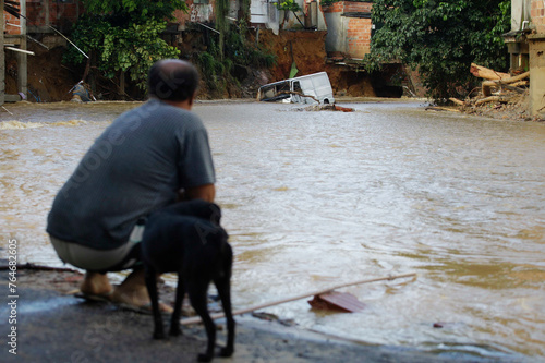 A man with his dog looks on a vehicle submerged in water during a big flood due to heavy rains in Duque de Caxias, Rio de Janeiro state, Brazil.