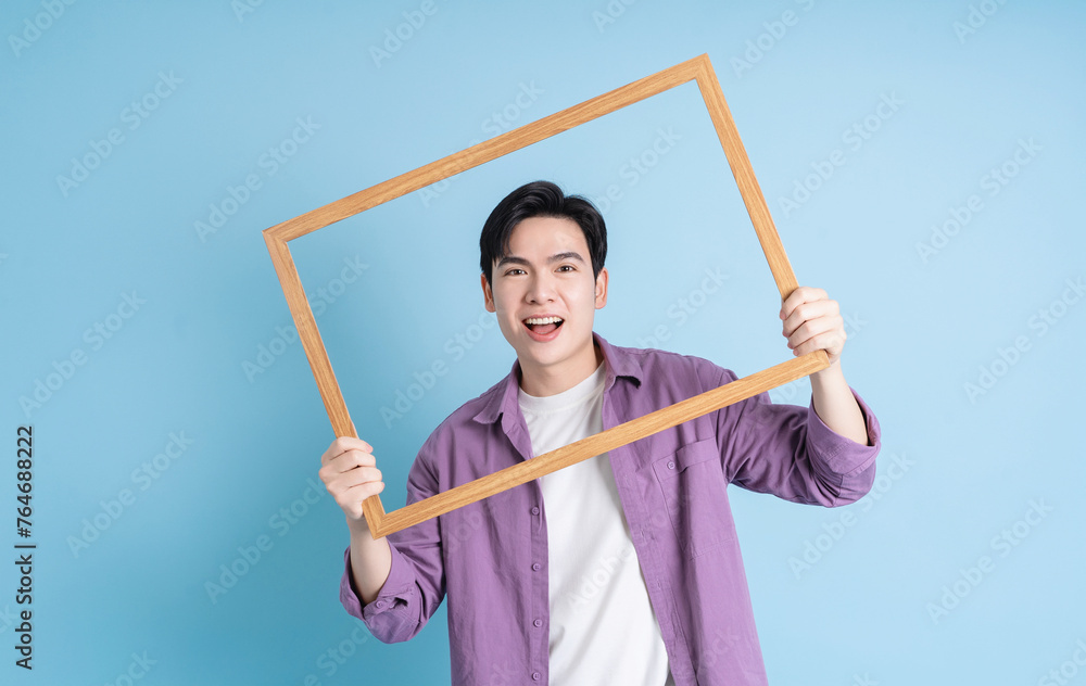 Young Ásian man holding photo frame on blue background