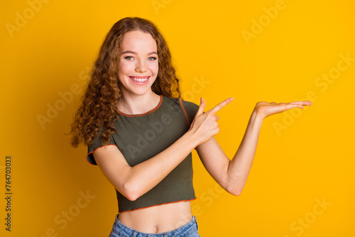 Photo of adorable cute girl wear stylish clothes arms demonstrate empty space logo brand isolated on yellow color background © deagreez