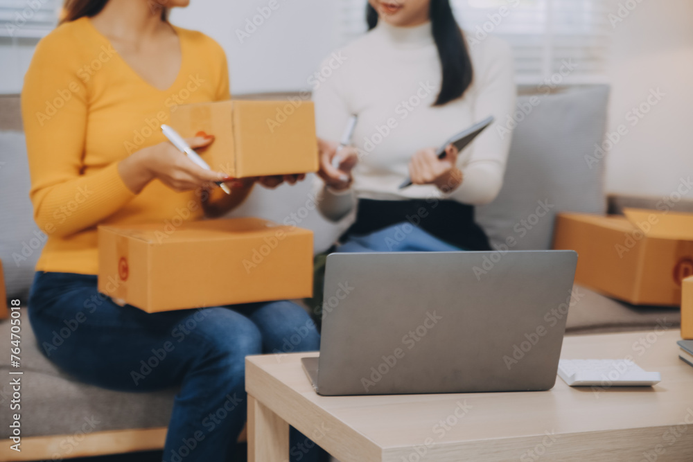 Asian SME business women use laptop computer checking customer order online shipping boxes at home. Starting Small business entrepreneur SME freelance. Online business, Work at home concept. Asian SME business women use laptop computer checking customer order online shipping boxes at home. Starting Small business entrepreneur SME freelance. Online business, Work at home concept.
