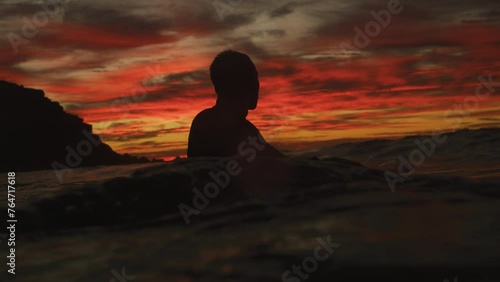 Medium shot of silhouette of man wading in water with board under red fire sunset sky