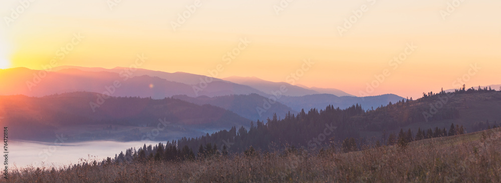 Majestic autumn scenery of foggy valley at Carpathian mountain range at early morning sunrise. Beautiful tonal perspective wide angle panorama.