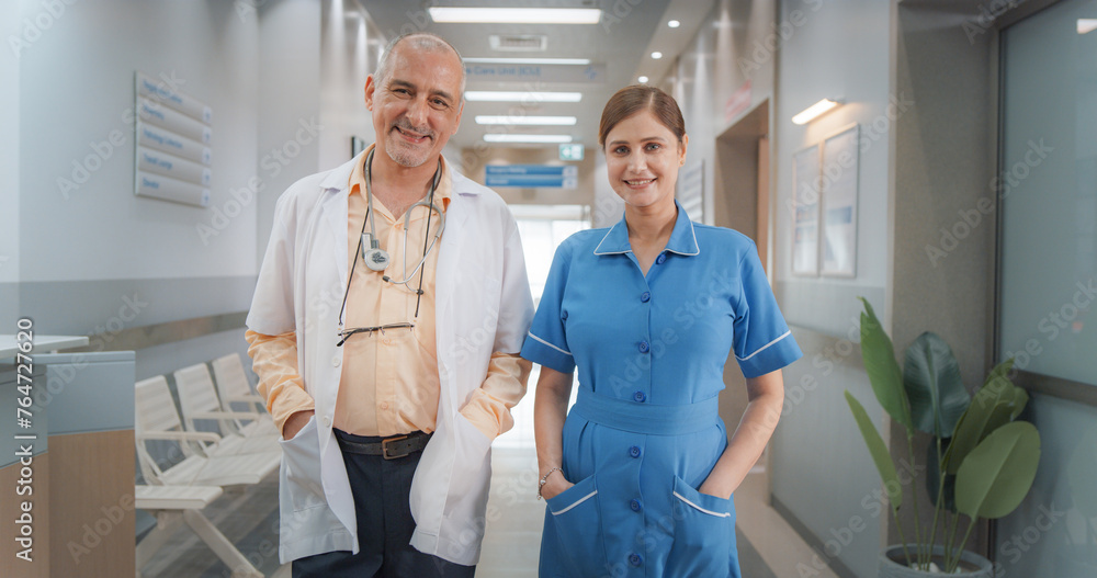 Fototapeta premium Two Friendly Indian Doctors: Team Portrait of Male Successful Medical Healthcare Professionals Standing in a Modern Hospital Office, Posing, Looking at Camera and Smiling. Doctor and Nurse on Duty
