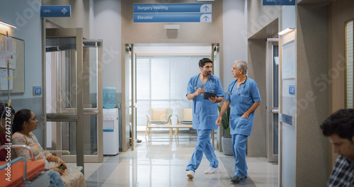 Portrait of Two Indian Male Doctors Walking in Hospital Corridor and Talking while Using a Digital Tablet. Two Medical Specialists Discussing the Treatment of a Patient