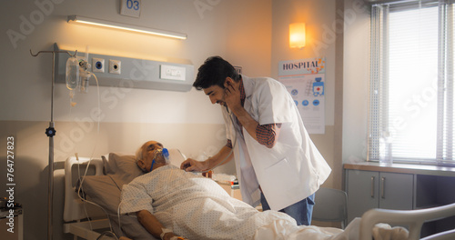 Portrait of a Young Intern Doctor Checking on his Elderly Patient with a Stethoscope in Modern Hospital. Nurse Checking Heart Rate of a Patient After Successful Surgery