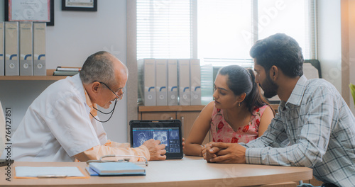 Portrait of Indian Couple Having a Doctor Appointment in Hospital. Professional Neurologist Using MRI Scan Images and Digital Tablet to Give Diagnosis and Suggestions to his Patient