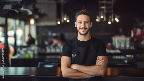 Portrait of a man barista in black t-shirt and apron behind counter in cafe.

 photo