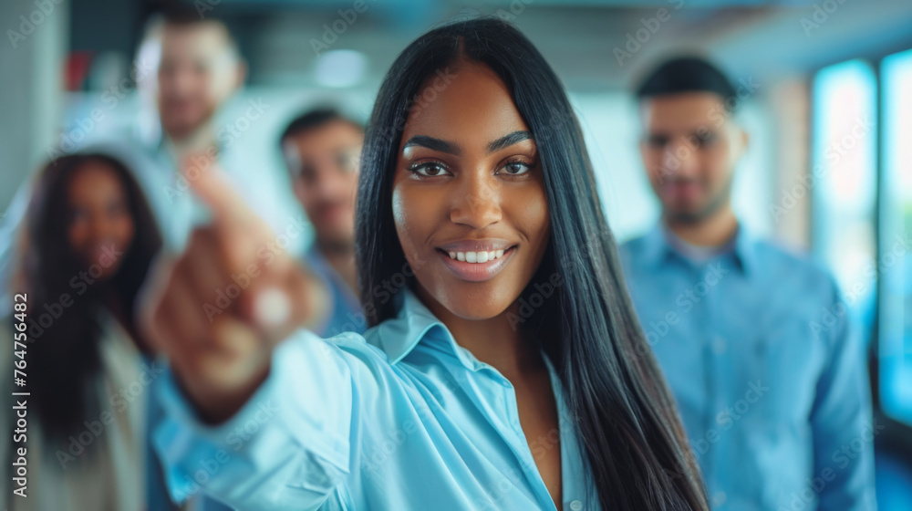 A confident woman with her hand extended as if to point or select, with a group of out-of-focus colleagues behind her. A confident woman with her hand extended as if to point or select, with a group of out-of-focus colleagues behind her.