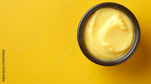 Bowl with melted butter or cheese on yellow background, top view, copy space. Dairy products photo