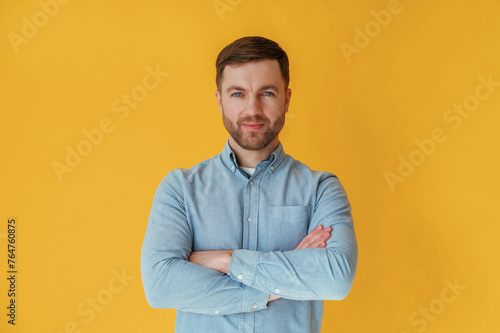 Standing with arms crossed. Attractive man in blue shirt is against yellow background © standret