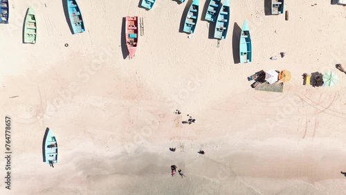 Many fishing boats on the shore of the tropical beach with palms, sand and ocean.Tourist umbrellas. People swim in the ocean. Caribbean Sea. Aerial top view photo