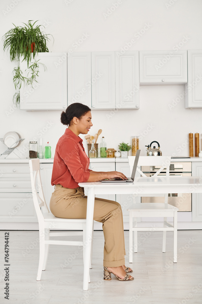 satisfied african american nutritionist using laptop while working remotely from her modern kitchen satisfied african american nutritionist using laptop while working remotely from her modern kitchen
