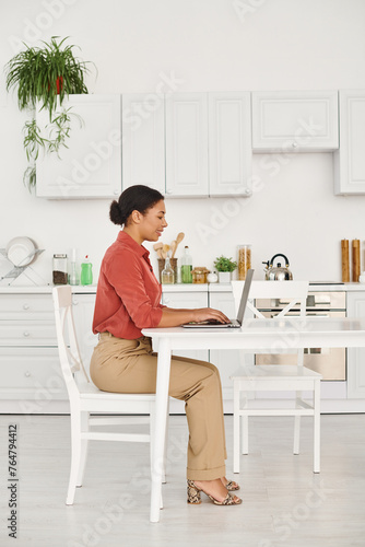 satisfied african american nutritionist using laptop while working remotely from her modern kitchen