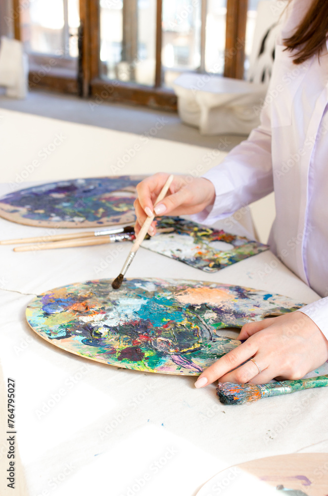 Woman artist in art studio holding brush and color palette. Painting process on vertical photo Woman artist in art studio holding brush and color palette. Painting process on vertical photo