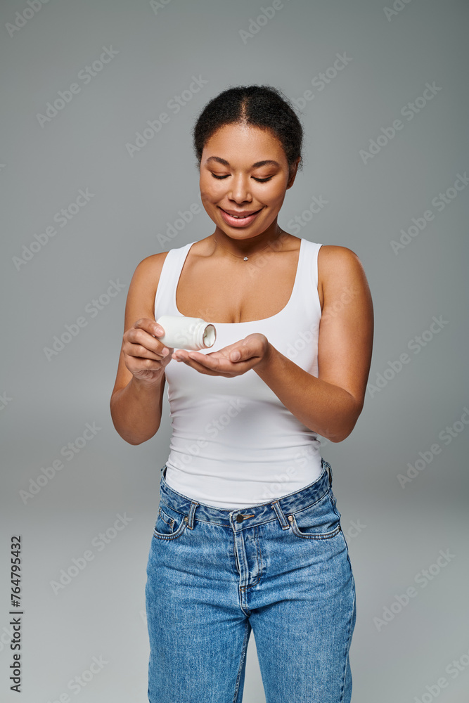 happy african american woman pouring pills from bottle into hand on grey background, dietary plan happy african american woman pouring pills from bottle into hand on grey background, dietary plan