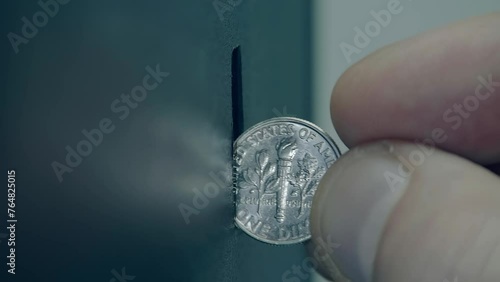 Male fingers inserting a 10 cent coin into a coin receiver, the light is brightly reflected from the surface of the coin. Closeup. Macro photo