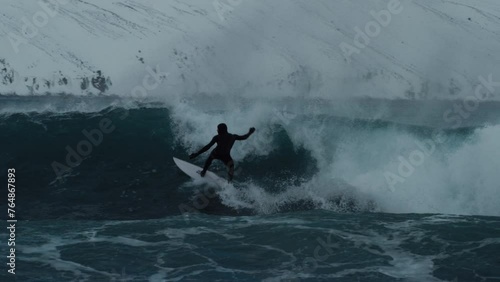 Surfer drops in to bottom turn cutting back and spraying water surfing in arctic with snow on mountains photo