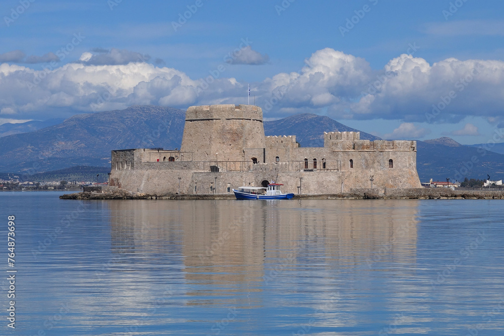 Beautiful small castle of Bourtzi built at sea a popular attraction in city of Nafplio former capital of Greece as seen at spring morning with nice white clouds and deep blue sky, Argolida, Greece