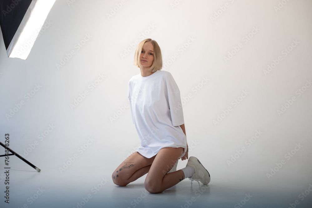 Fototapeta premium Beautiful girl in a white oversized t-shirt posing on a white background. Posing sitting on the floor.