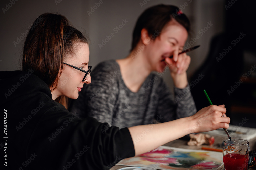 Fototapeta premium Two friends share laughter and joy while engaged in watercolor painting, illustrating the pleasure of artistic hobbies.