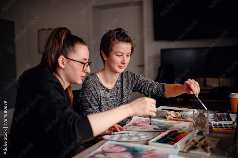 Two artists deeply focused on their watercolor techniques, a synergy of concentration and creativity fills the room