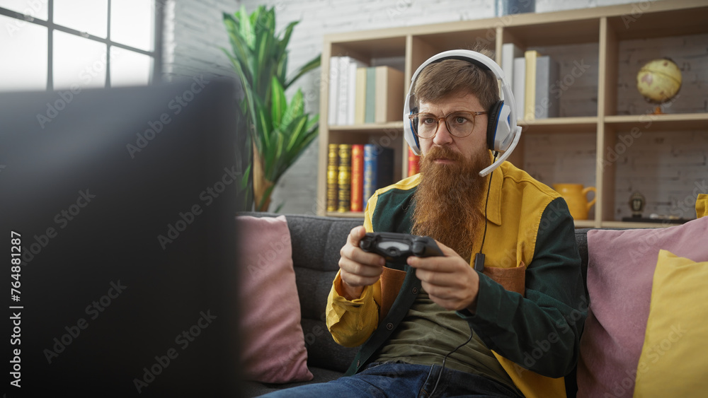 Focused man with beard and glasses playing video games indoors, showcasing a cozy lifestyle and entertainment.