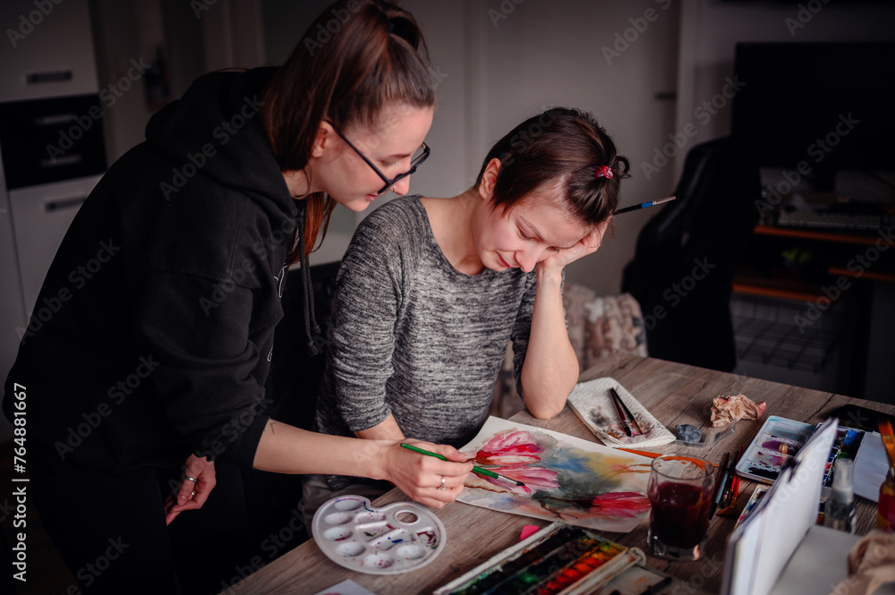 A moment of creative consultation, as one artist guides another, their collective focus on the watercolor artwork unfolding before them