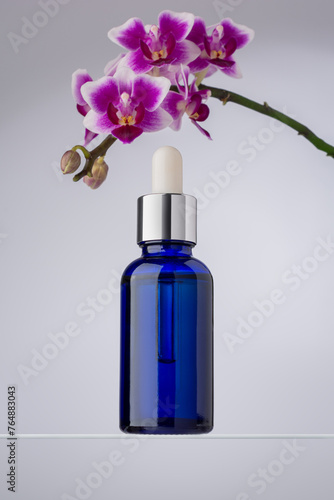 An elegant blue glass dropper bottle, placed beside blooming purple orchids