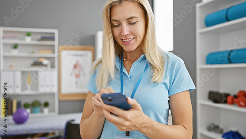 Blonde woman using smartphone in clinic interior, embodying healthcare, technology, and professionalism.