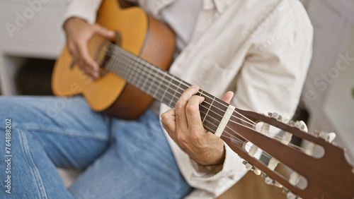 A young adult man plays an acoustic guitar in a well-lit indoor setting, exuding a casual and artistic atmosphere. photo