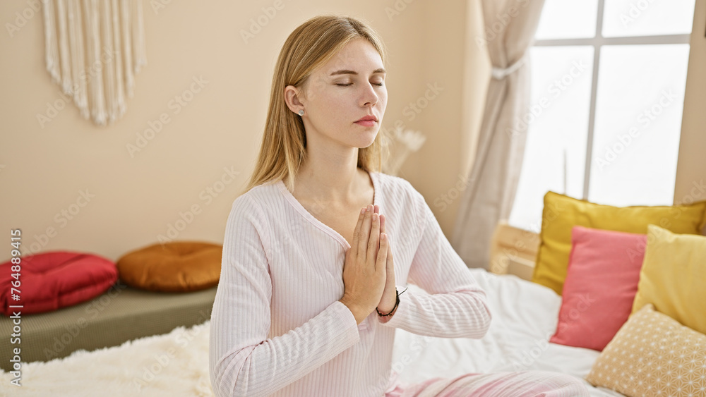 A serene blonde woman meditates in a cozy bedroom, embodying tranquility and mindfulness. A serene blonde woman meditates in a cozy bedroom, embodying tranquility and mindfulness.