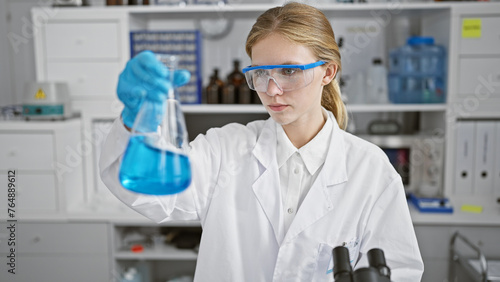 Blonde woman scientist examining a blue liquid in a flask in a laboratory setting