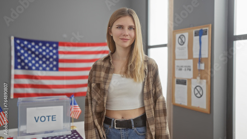 A young blonde woman stands confidently in a usa voting center adorned with flags and informational posters. photo