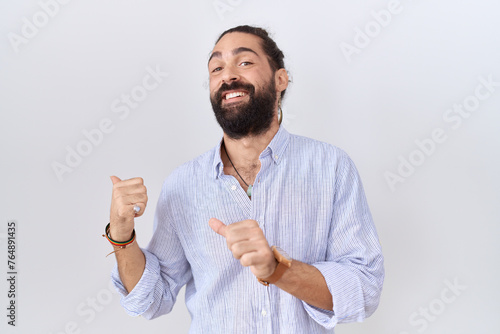 Hispanic man with beard wearing casual shirt pointing to the back behind with hand and thumbs up, smiling confident